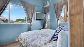 Ein Schlafzimmer mit Bett, Vorhängen, Fernseher und einem Fenster mit Blick ins Freie.