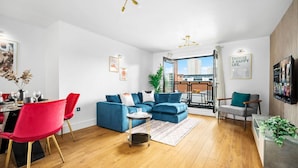 A modern living room with a blue sofa, red chairs, and a dining area with a table set for four. - 2 Bed Apartment - City Centre - Parking - Balcony
 (Birmingham)