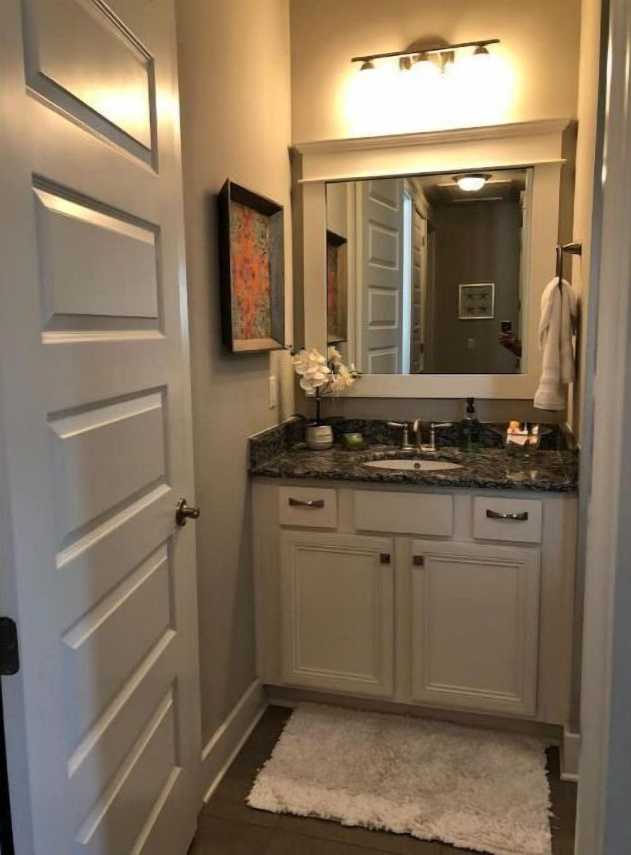 Une petite salle de bain avec une porte blanche, un meuble-lavabo avec un évier, un miroir et un petit tapis sur le sol.