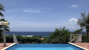 A rectangular swimming pool with a clear view of the ocean and a distant cityscape.