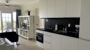 A modern kitchen with white cabinets, a black countertop, and a built-in oven. There is a dining area with a black chair and a white table.