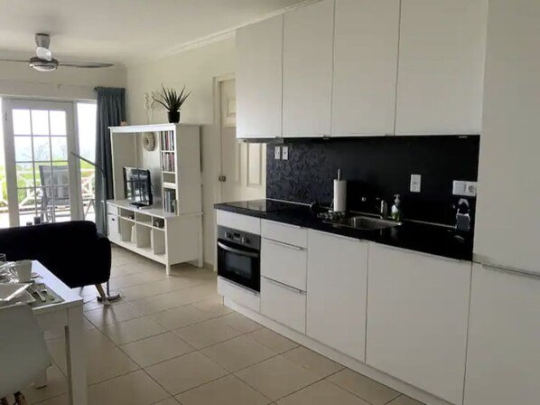 A modern kitchen with white cabinets, a black countertop, and a built-in oven. There is a dining area with a black chair and a white table.