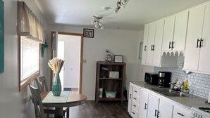 Cocina compacta con armarios blancos, una mesa de comedor con sillas, microondas y estufa.