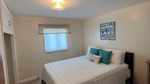 Un dormitorio con cama, una ventana con persianas, una lámpara de pared y una frase motivacional en la pared.