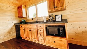 A kitchen with wooden cabinets, a microwave, and a window above the sink.