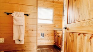 A wooden cabin interior with a toilet, a towel hanging on a rack, a window, and wooden cabinets.