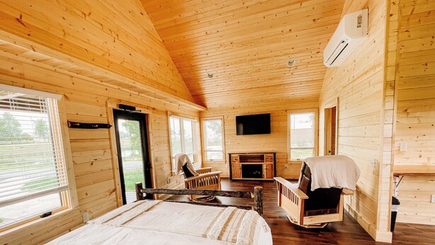 A log cabin room with a bed, a fireplace, a television, and a window with blinds.