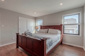 A bedroom with a wooden bed, a nightstand, a lamp, and a window with blinds.