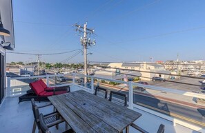 A balcony with a wooden table and red chairs, overlooking a street with buildings and a bridge.