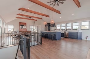 A spacious kitchen with wooden beams, a central island, pendant lighting, and large windows.