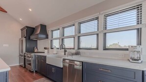 Eine moderne Küche mit Edelstahlgeräten, einem großen Fenster mit Jalousien und Blick auf die Stadt.