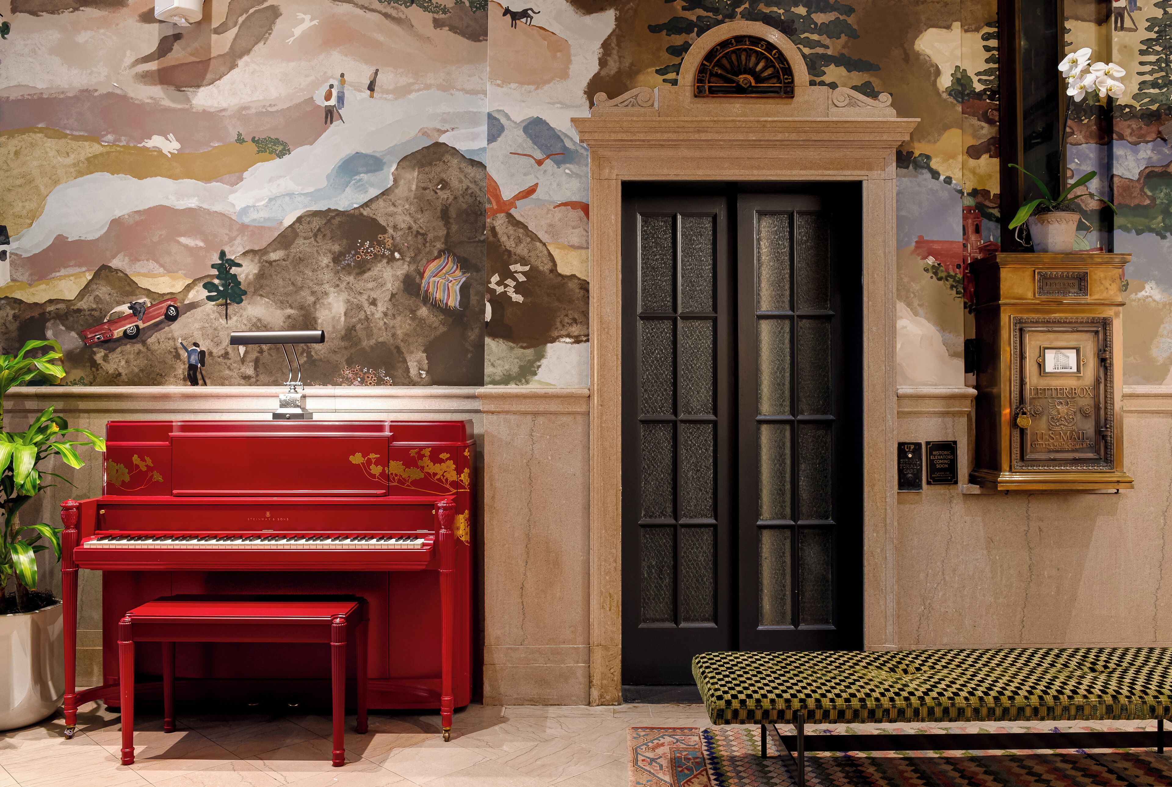 Um piano vermelho, um banco, uma porta e um mural com várias figuras e paisagens.