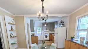 A modern kitchen with a glass dining table, white chairs, wooden cabinets, and a chandelier. - Center of Wilmington-Zen on 42nd-fully fenced yard-Pets ok (Wilmington)