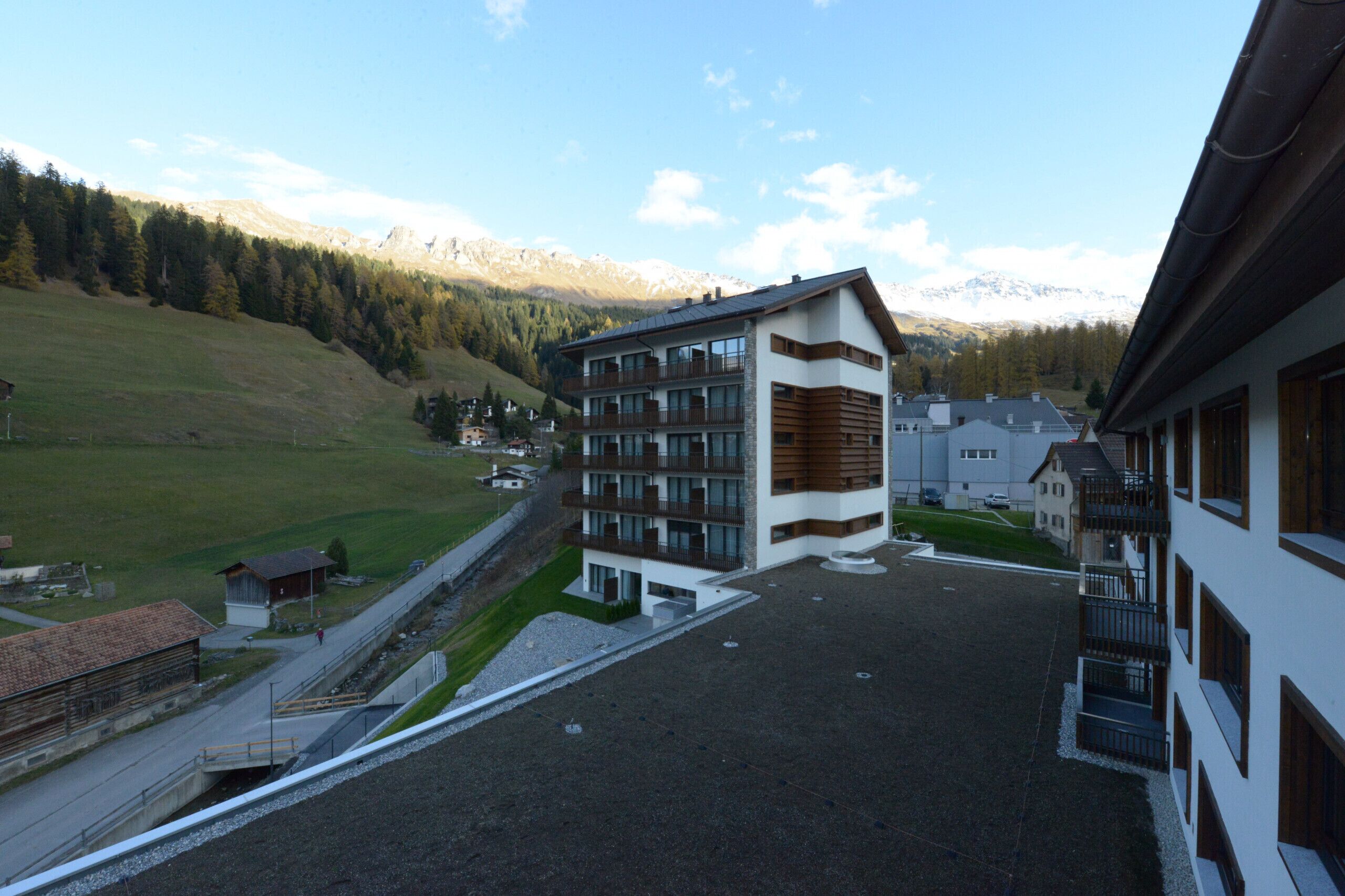 Un hôtel moderne à l’architecture imposante, avec plusieurs étages, un parking et une vue sur un paysage montagneux.