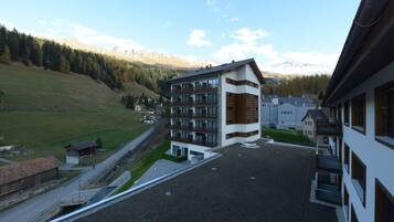 Un hôtel moderne à l’architecture imposante, avec plusieurs étages, un parking et une vue sur un paysage montagneux.