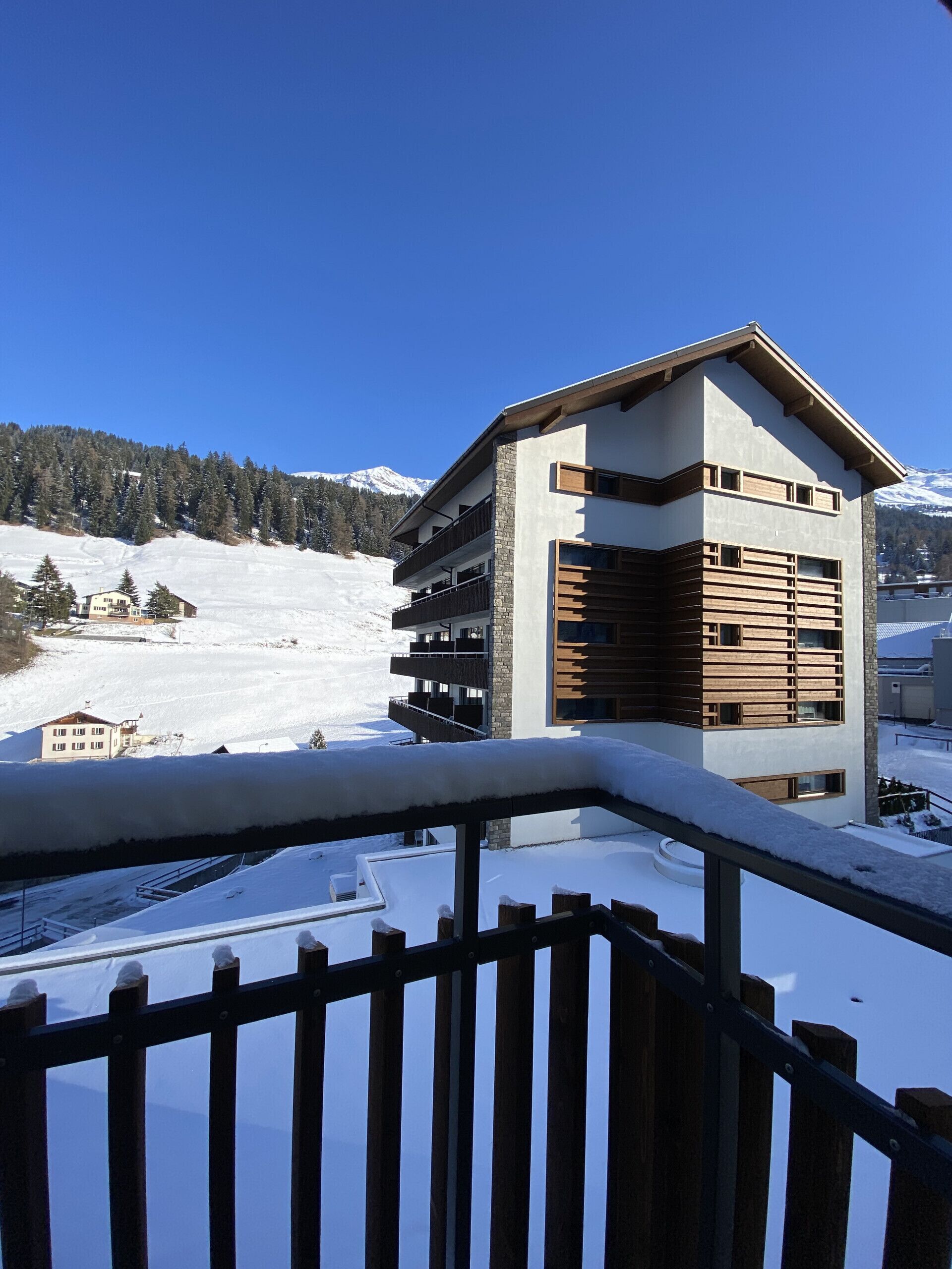 A modern multi-story building with balconies, set against a snowy mountain backdrop.