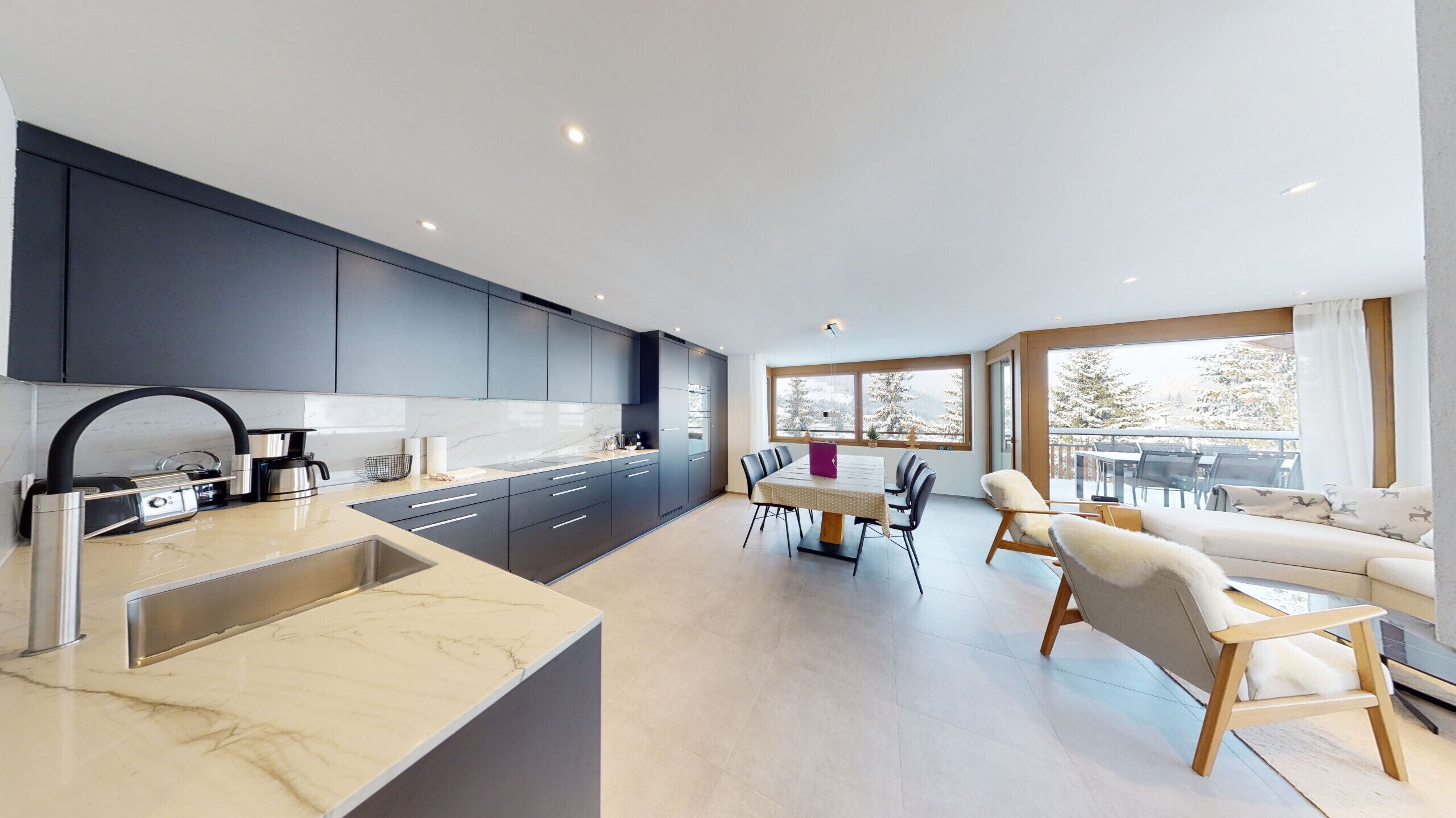 A modern kitchen with dark cabinets, a marble countertop, and a dining area with a table and chairs.
