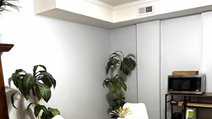 A dining area with a glass table, white chairs, wooden flooring, and potted plants.