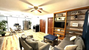 A living room with a sofa, armchair, ottoman, and a TV stand with shelves.