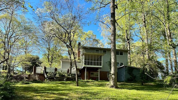 A two-story house with a front porch, surrounded by trees and a grassy yard.
