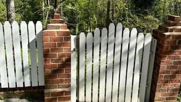 Une porte en treillis blanche, avec des piliers en briques, qui mène à un chemin pavé.