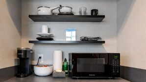 Eine Küche mit Mikrowelle, Kaffeemaschine und Regalen mit Küchenutensilien.