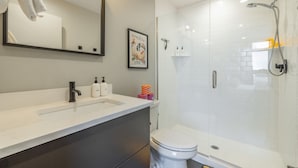 Ein modernes Badezimmer mit einem weißen Waschbecken, dunklen Schränken, einer Toilette und einer Duschkabine.