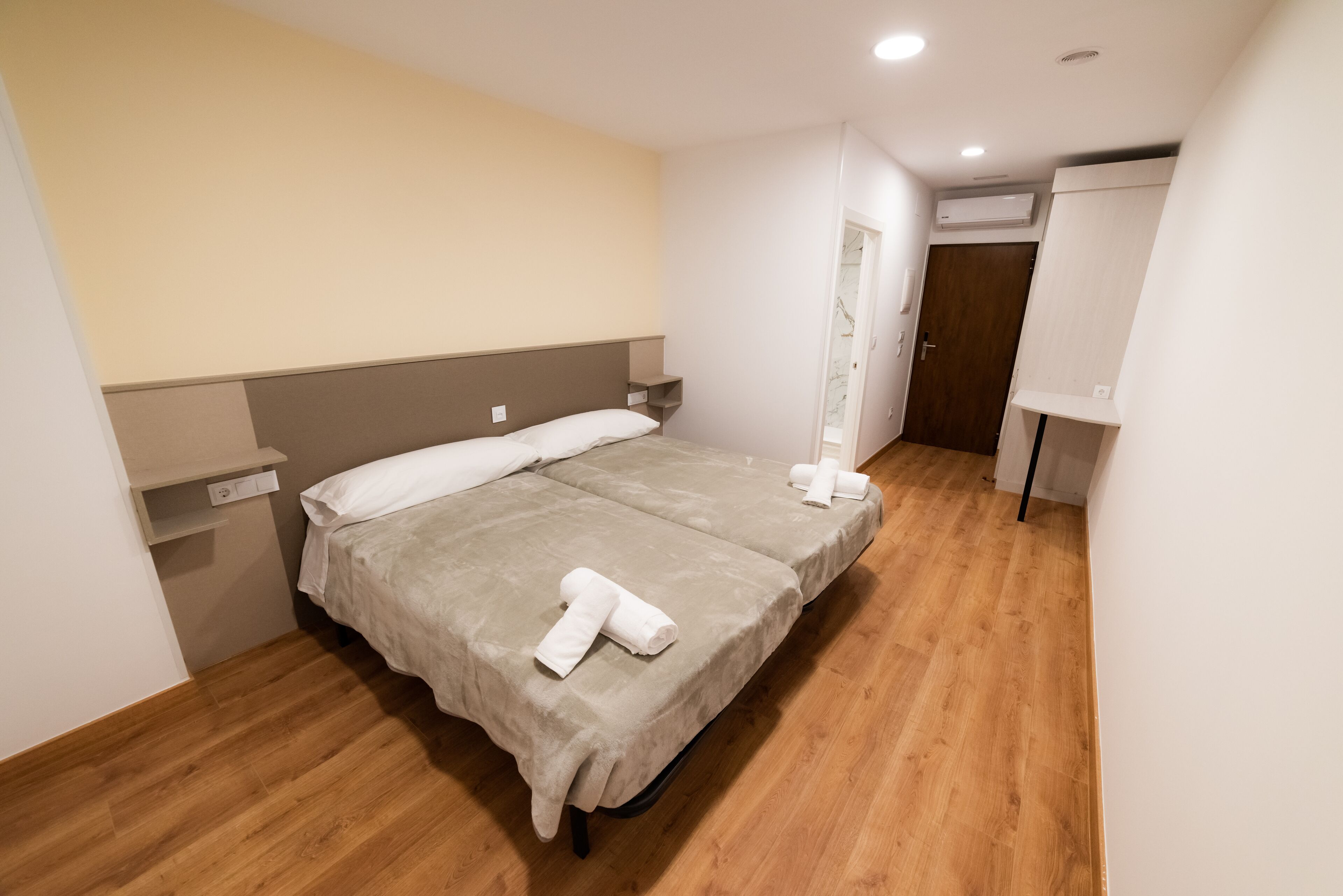 A hotel room with a double bed, a bedside table, a wardrobe, and a wooden floor.