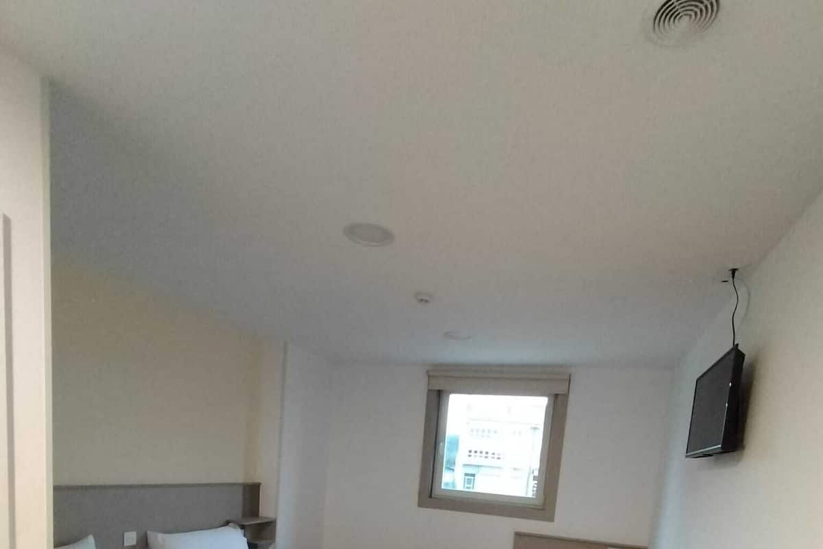 A room with three single beds, a small window, a TV on the wall, and a wooden floor.