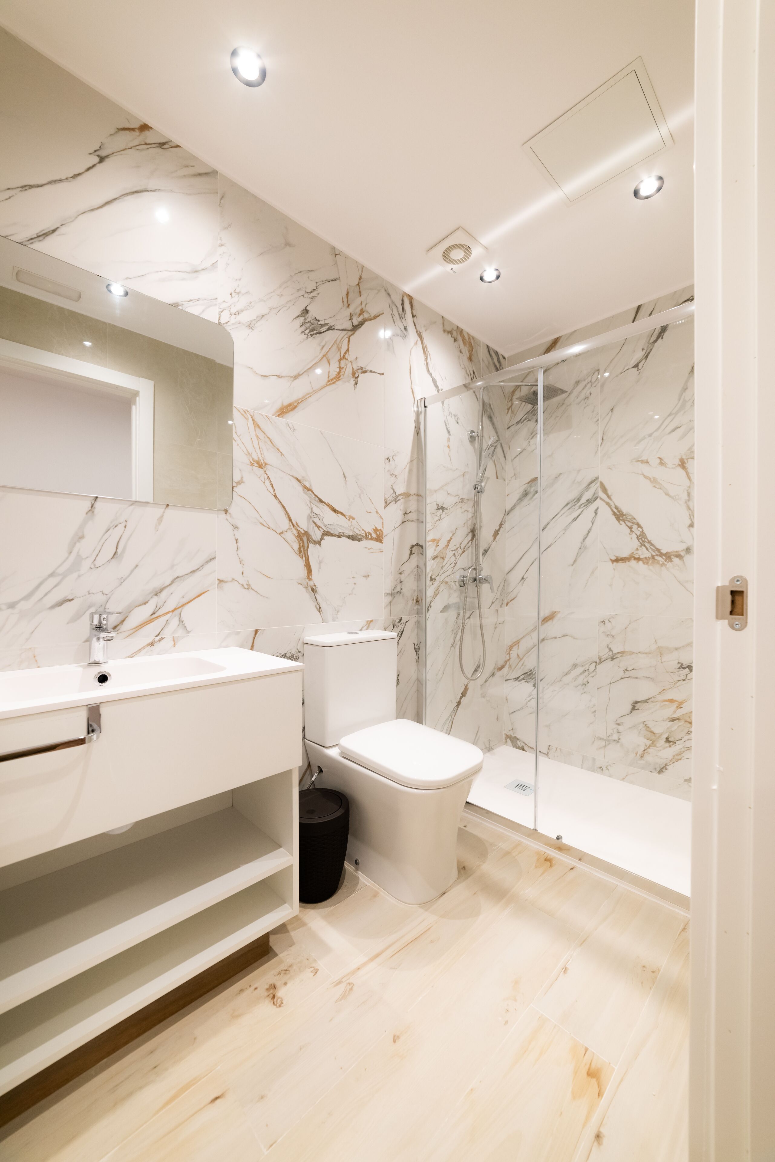 Un baño moderno con paredes de mármol, un lavabo blanco y una cabina de ducha de vidrio.