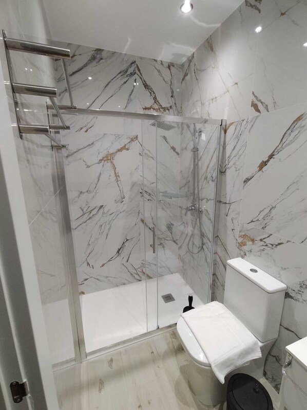Et moderne badeværelse med et brusebad bag glas, toilet og håndvask.