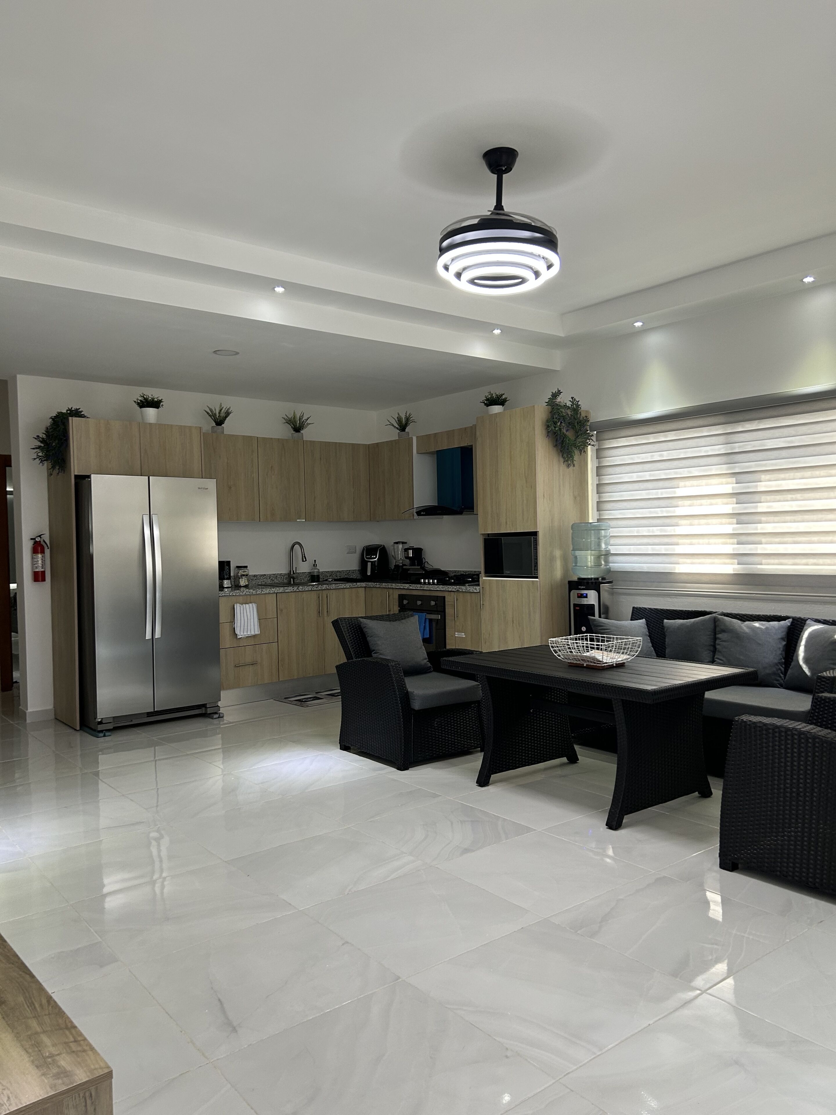 A modern kitchen with a built-in refrigerator, wooden cabinets, and a dining area with a black table and chairs.