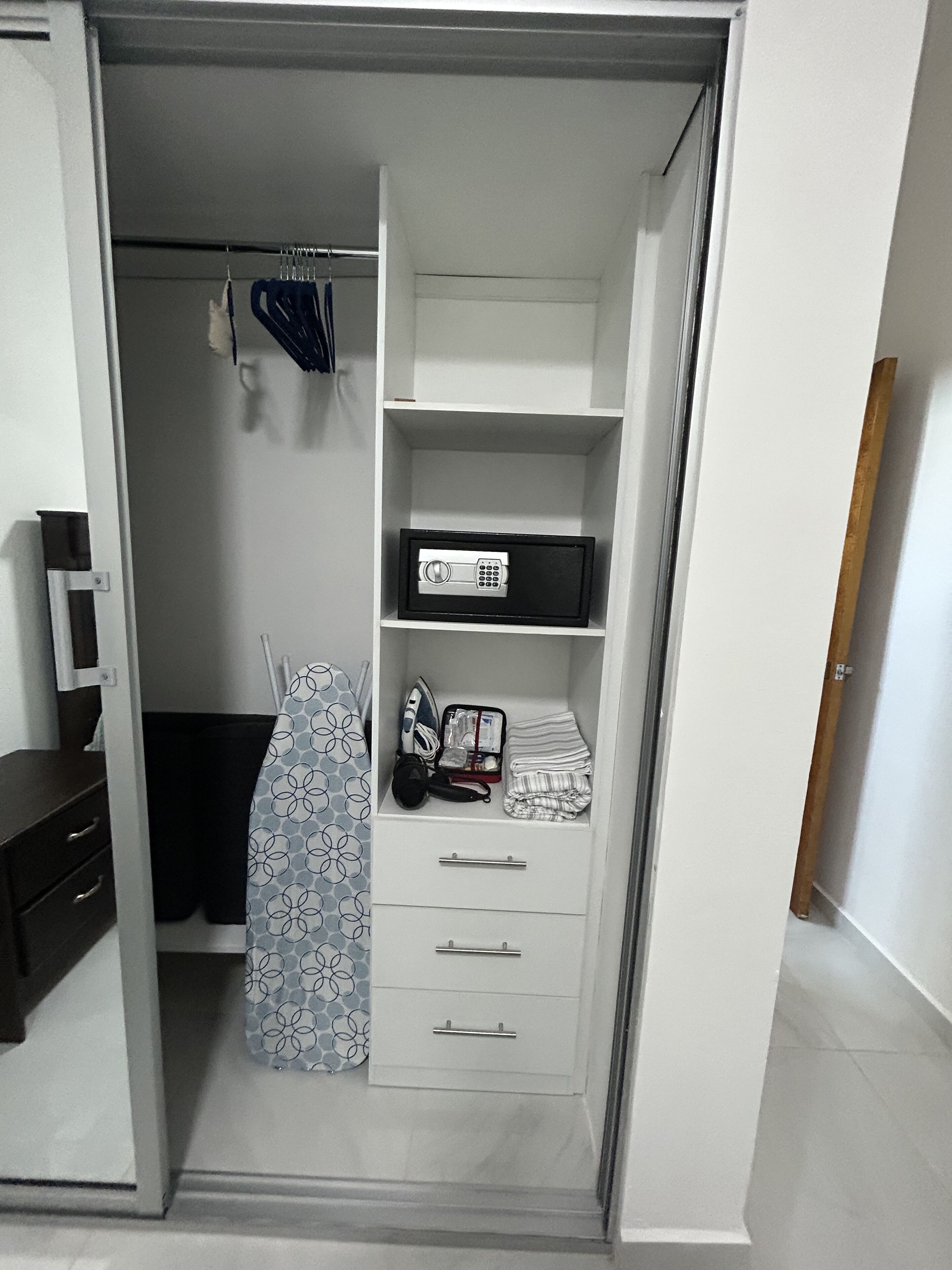 A walk-in closet with open shelving, a hanging rack, and a folded ironing board.