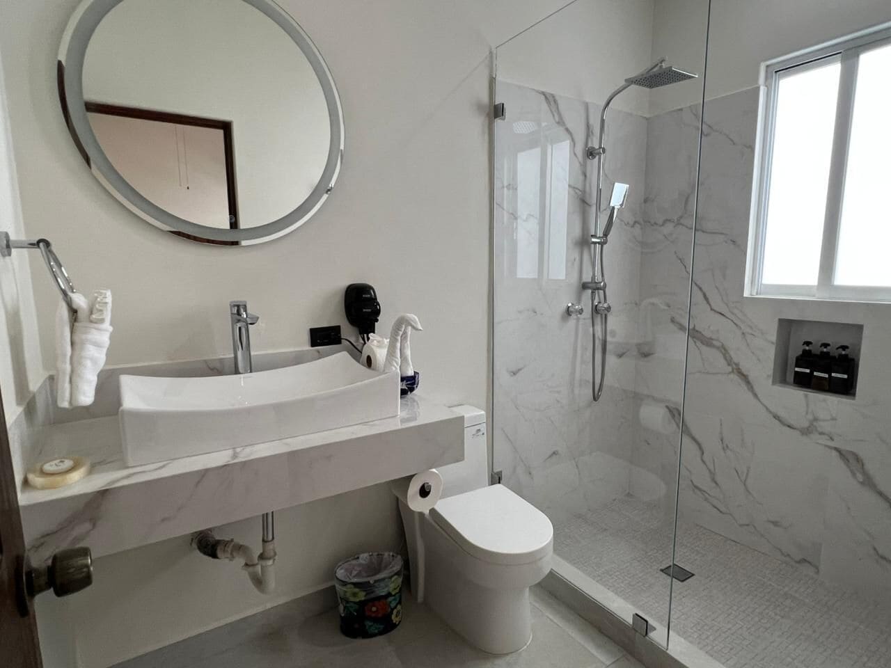 Un baño moderno con ducha de vidrio, lavamanos blanco y retrete.