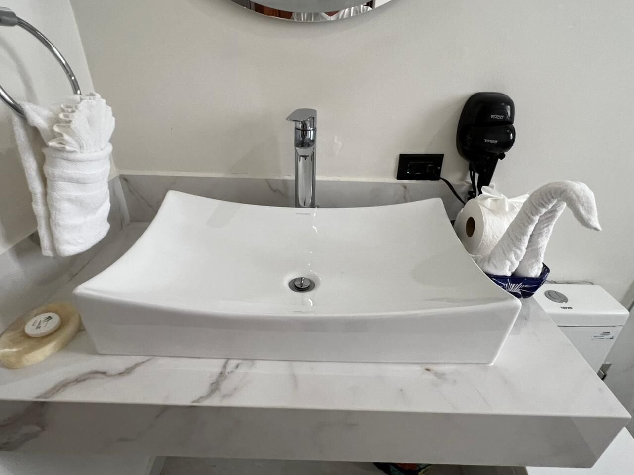 A bathroom with a white sink, a towel rack, a hairdryer, and a soap dish.