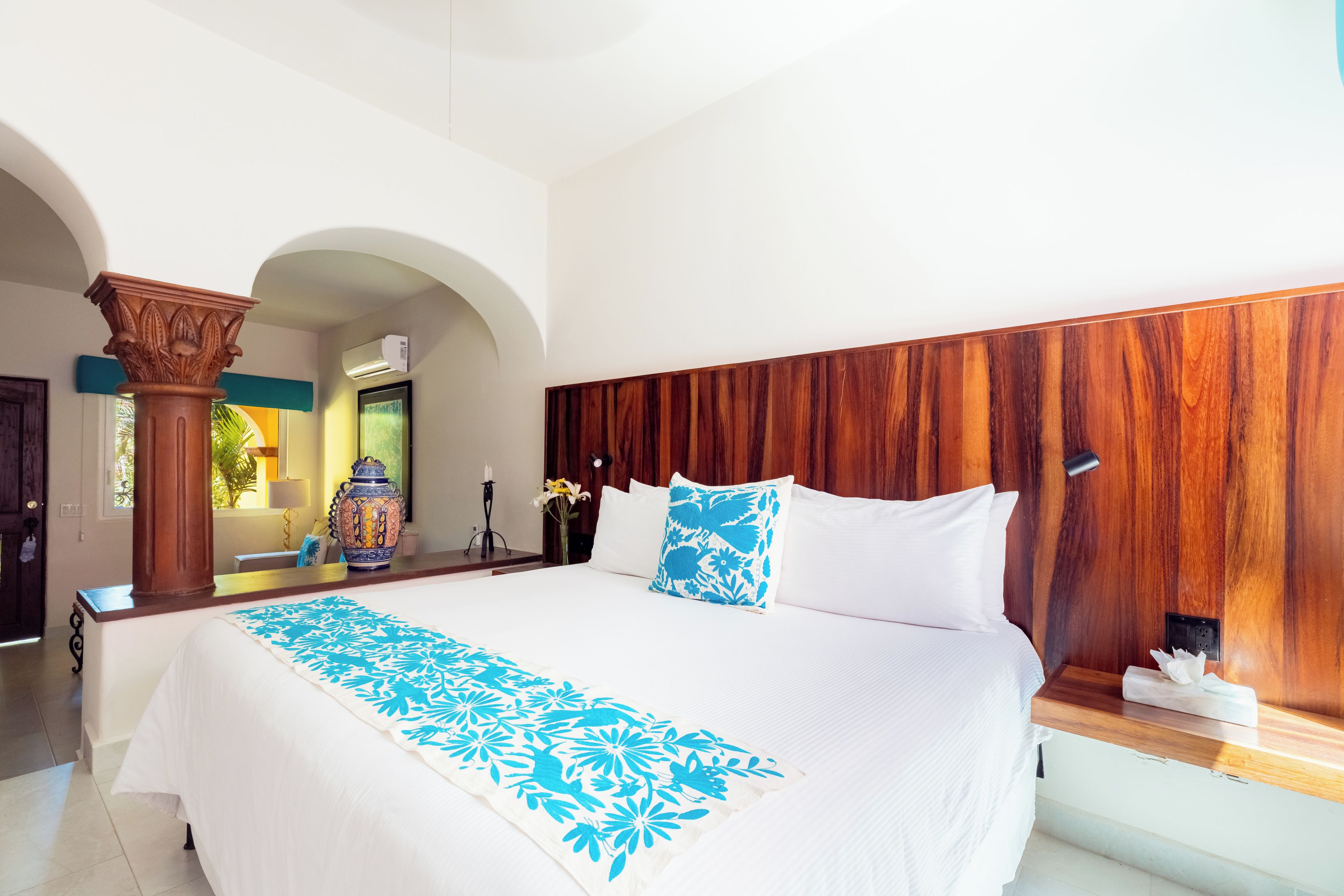 Une chambre d’hôtel avec un grand lit, une tête de lit en bois, un vase décoratif et une fenêtre donnant sur un beau paysage.