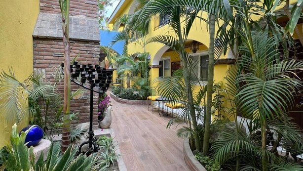 A courtyard with a wooden pathway, yellow buildings, and various plants. - El Encanto Inn (San José del Cabo)