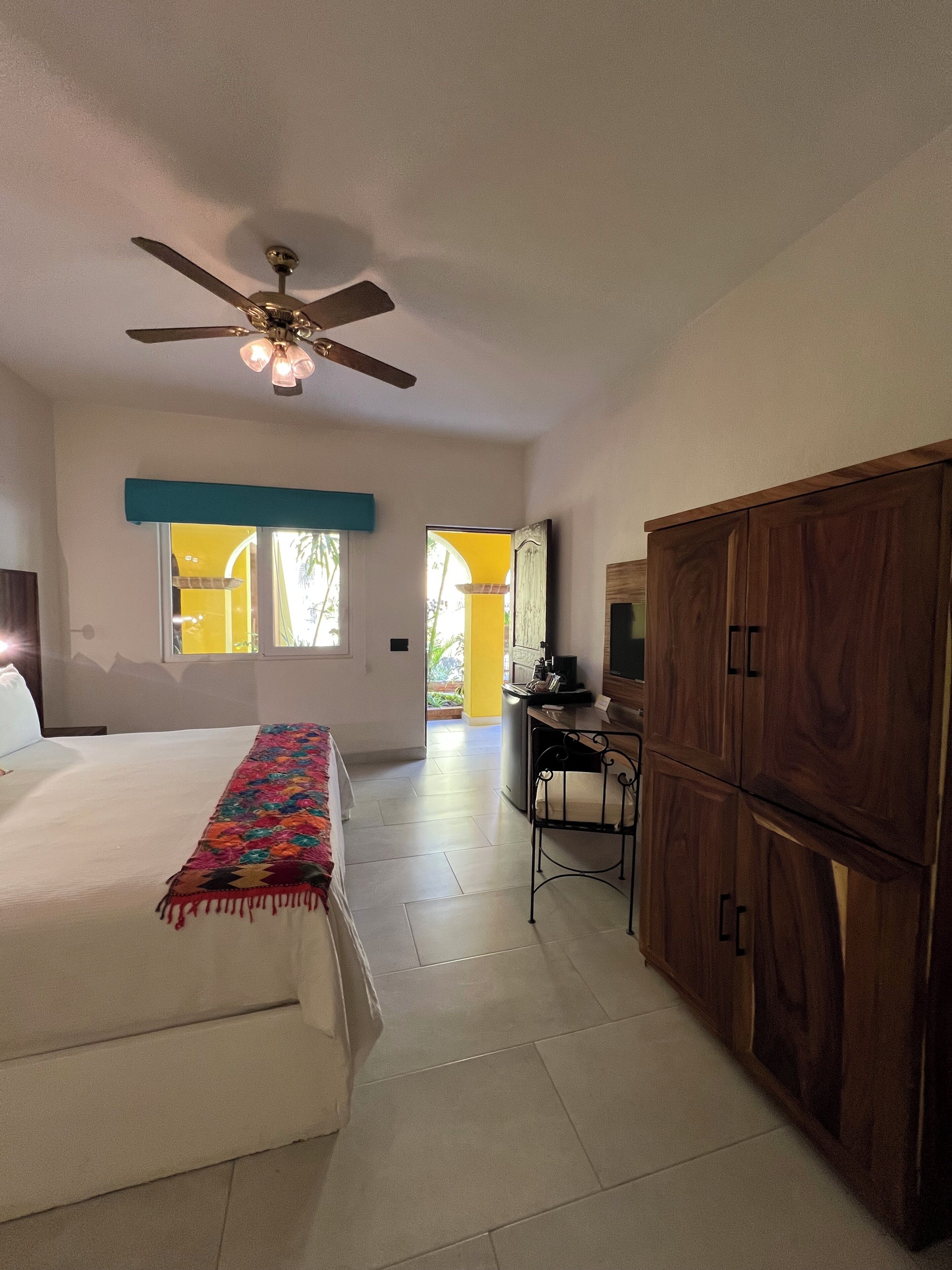 A bedroom with a bed, a desk, a wardrobe, and a ceiling fan.