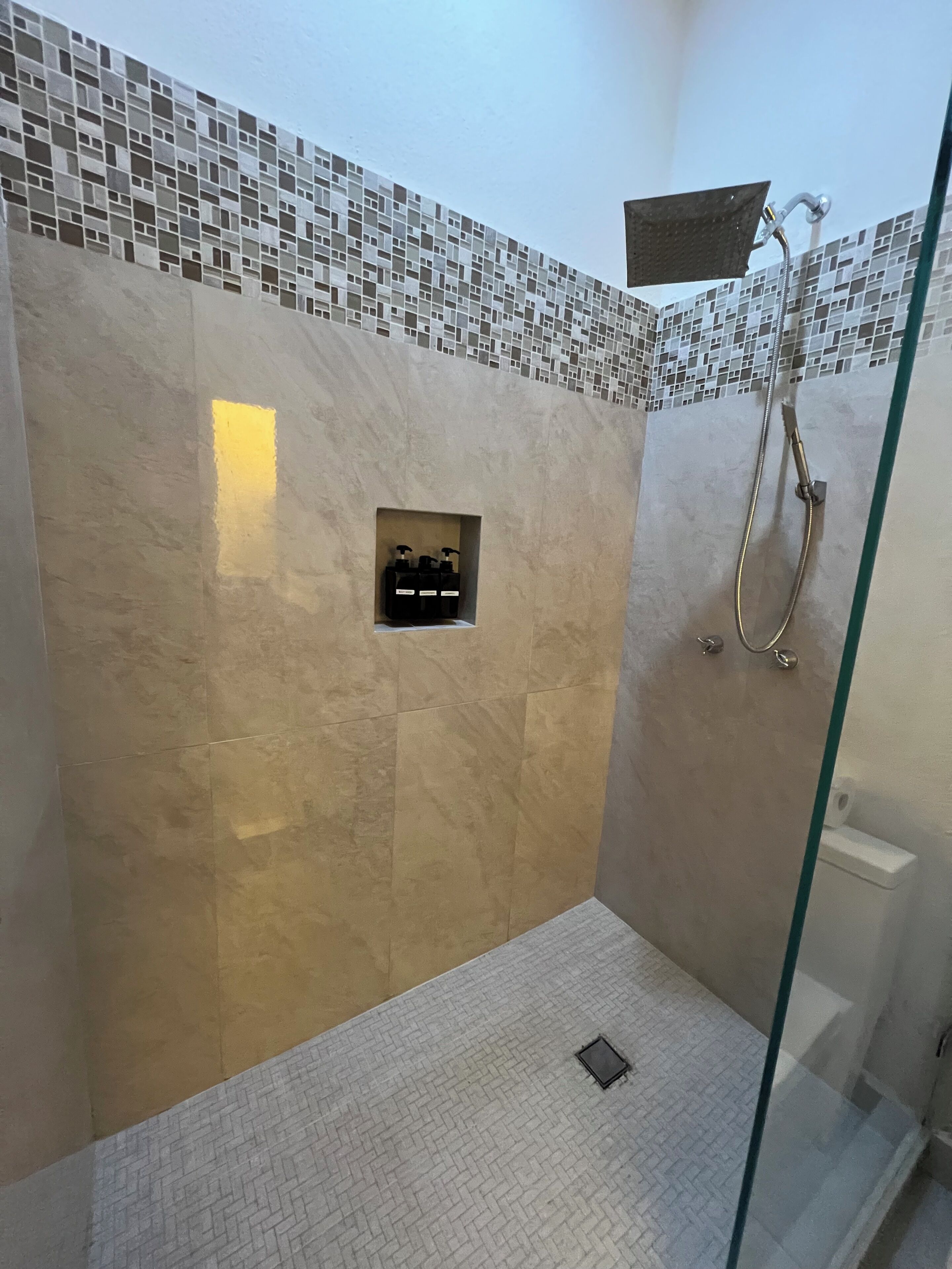 A shower area with a glass door, a tiled wall, and a small shelf with toiletries.