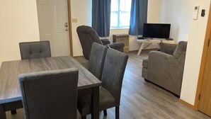 Un soggiorno moderno con angolo da pranzo, arredamento grigio, televisore a schermo piatto e finestra con tende.