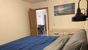 Una camera da letto con un letto, una cassettiera, una scrivania con sedie e un quadro appeso al muro.