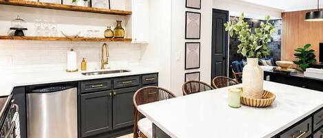 A modern kitchen with dark cabinetry, a central island, and a dining area with chairs.