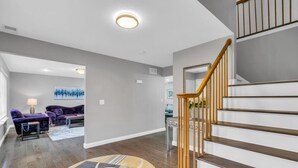 A modern living room with a staircase, hardwood flooring, and a cityscape painting on the wall. - 5 Bedroom Lavish Summer Oasis with Inground Pool (Ocean Township)