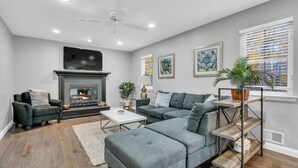 A modern living room with a fireplace, grey sofas, a coffee table, and artwork on the walls. - 5 Bedroom Lavish Summer Oasis with Inground Pool (Ocean Township)