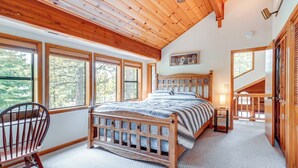 A bedroom with a wooden bed, large windows, a chair, and a small bedside table. - Deck w/ New Hot Tub (Old Pic): Large TD Home (Truckee)