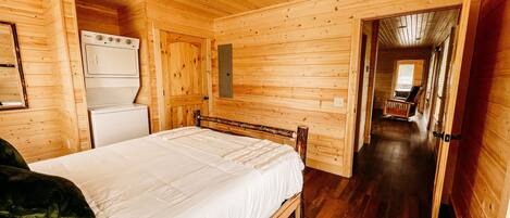 Une pièce de type cabane en bois, comprenant un lit, une petite kitchenette et un couloir menant à une autre pièce.