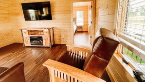 Ein gemütliches Blockhaus-Interieur mit Holzausbau, Kamin, Fernseher und einem Fenster mit Jalousien.