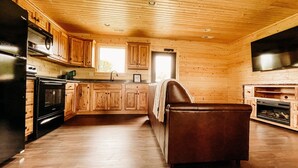Eine Küche mit Holzausstattung, einem schwarzen Kühlschrank, einem Herd und einem braunen Ledersessel.