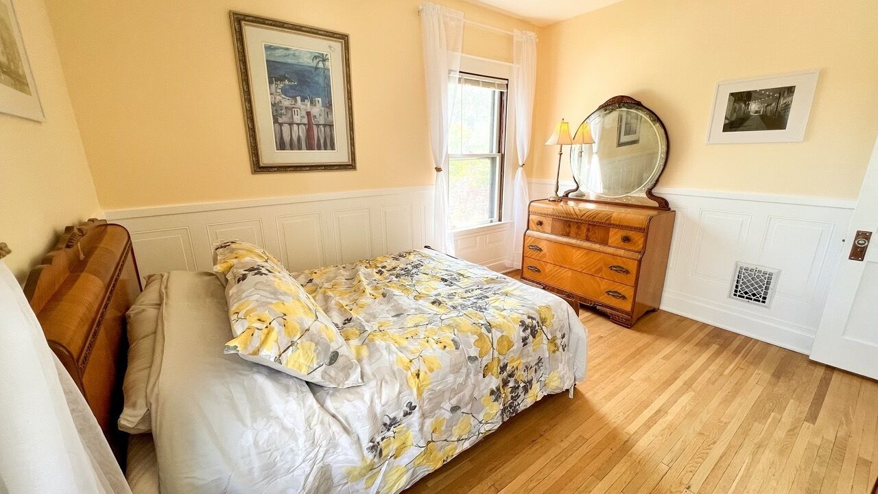 Un dormitorio con cama, cómoda y ventana con cortinas.