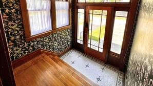 A room with a wooden floor, a patterned wallpaper, and a large window with curtains. - The Antique Reno is walking distance to the Falls and in a historic area. (Niagara Falls)